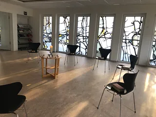 Heller Raum mit großen, abstrakten Buntglasfenstern und Stühlen.