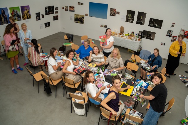 Eine Gruppe von Menschen sitzt an Tischen in einem Raum, der mit Fotos geschmückt ist.