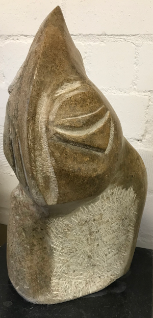 Abstrakte Steinskulptur mit geriffelten und glatten Texturen vor einer Backsteinwand.