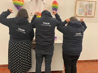 Drei Personen von hinten, mit Kapuzenpullovern und der Aufschrift "TEAM".