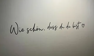 Handgeschriebener Text auf hellem Untergrund: „Wie schön, dass du da bist.“