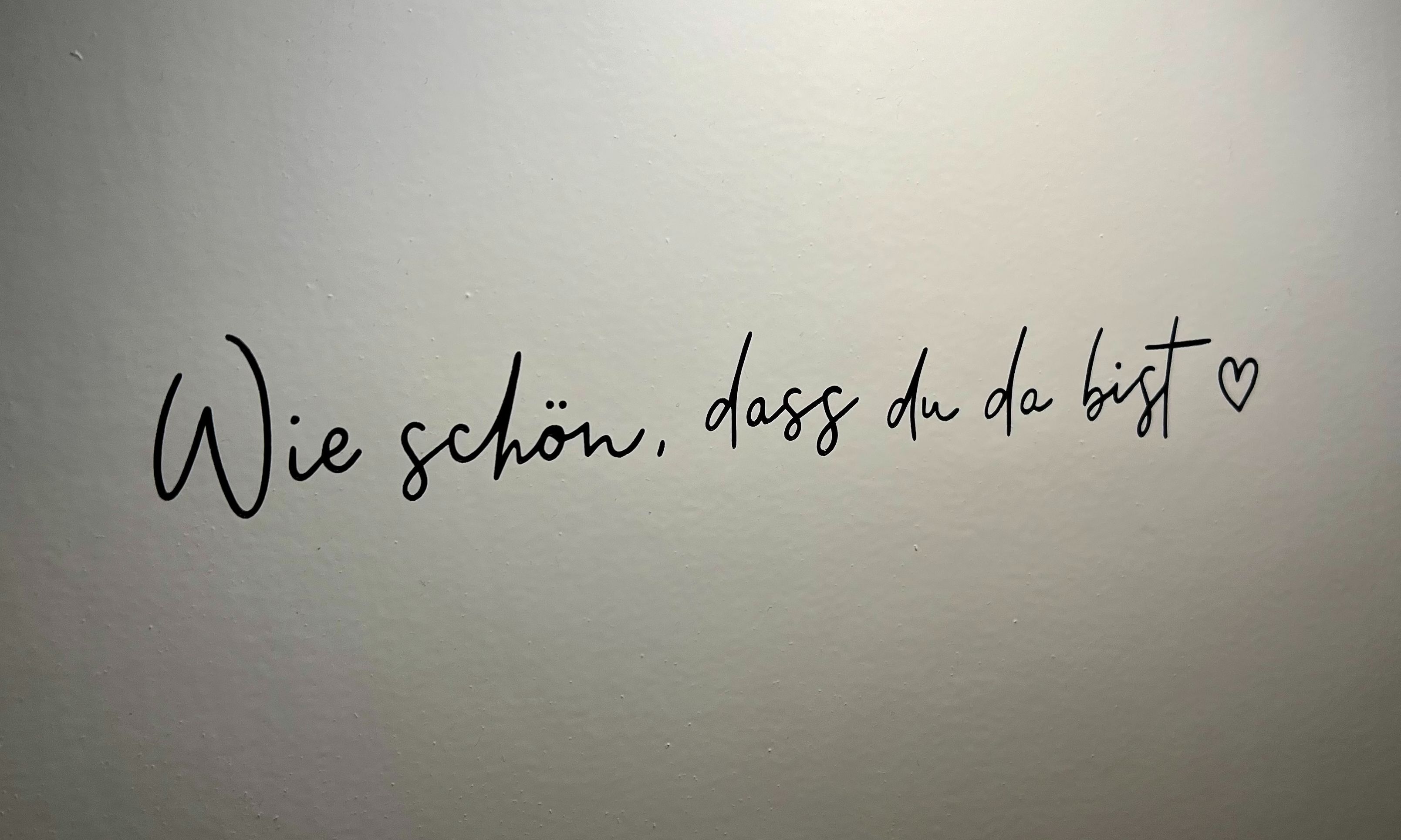 Handgeschriebener Text auf hellem Untergrund: „Wie schön, dass du da bist.“