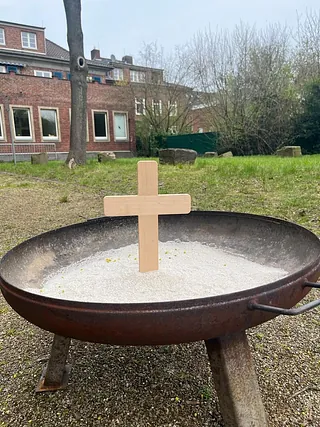 Holzkreuz in einer Schale mit Sand im Freien.