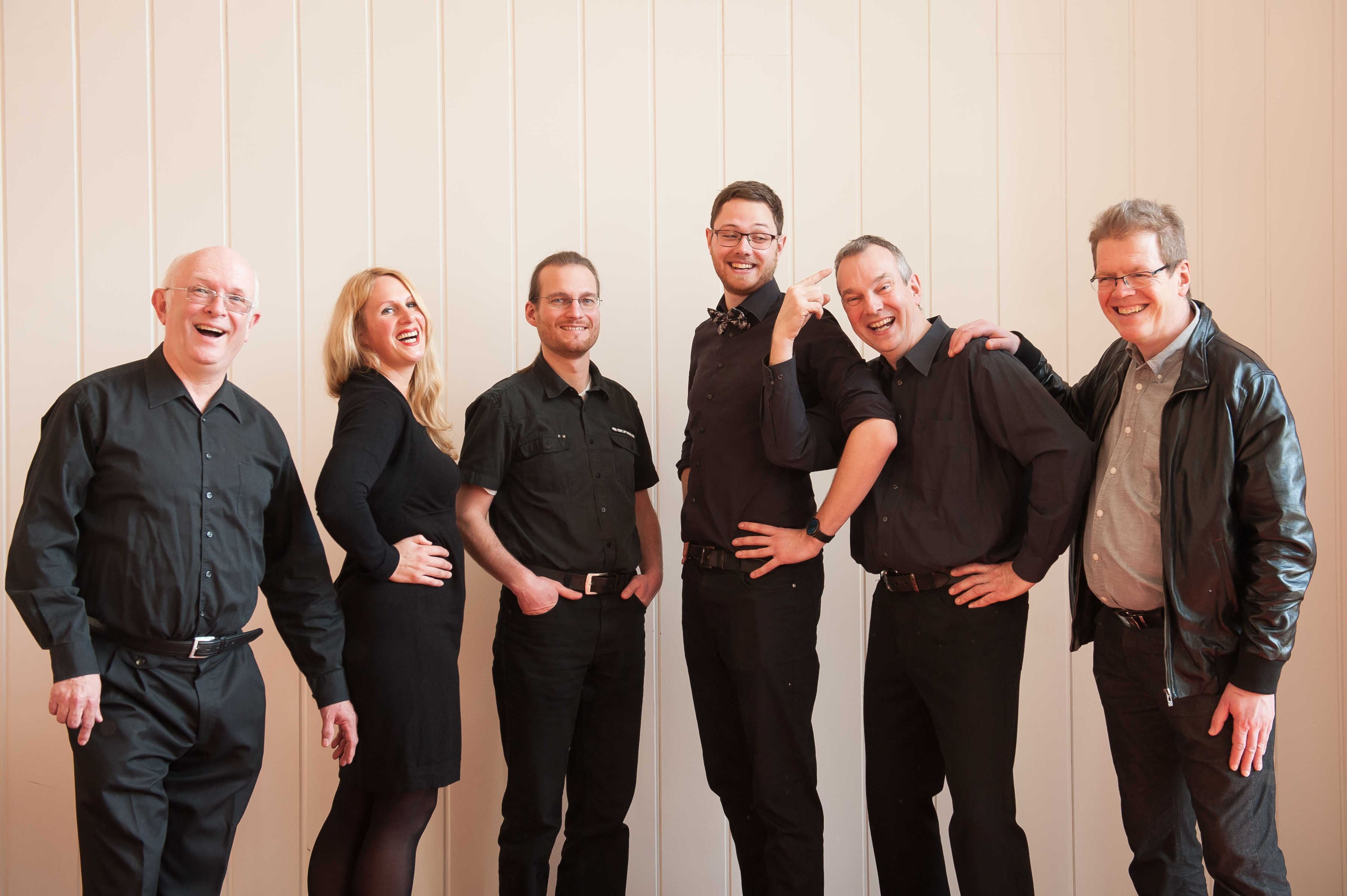 Gruppe von sechs lächelnden Bandmitgliedern posiert im Stehen.