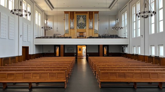 Heller Kircheninnenraum mit Orgel und Holzbänken.