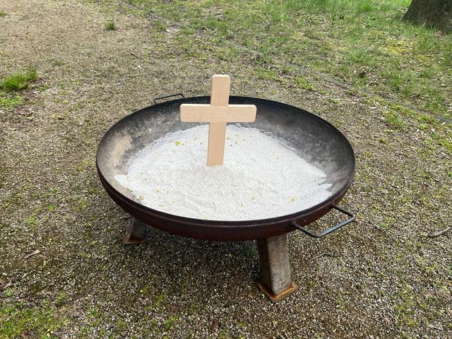 Holz-Kreuz in einer Schale mit weißem Sand im Freien.