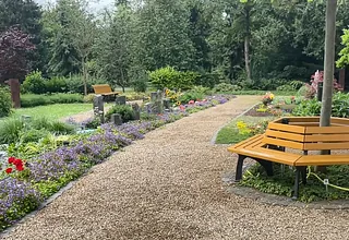 Kiesweg in einem blühenden Garten mit einer Bank.