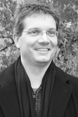 Schwarz-Weiß-Porträt eines lächelnden Mannes mit Text zu „Die Unsichtbaren“.