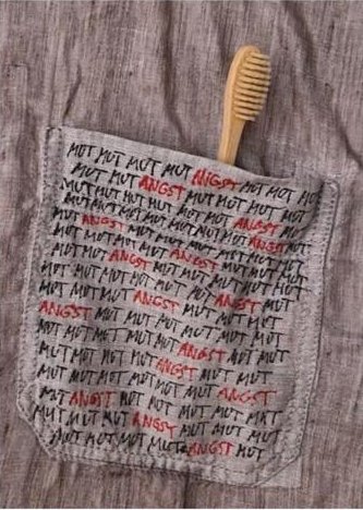 Hemdtasche mit Holzzahnbürste und wiederholtem Text „MUT“ (Mut) und „ANGST“ (Angst) darauf.