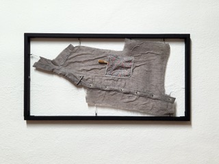 Graues Hemd mit Stift in der Tasche, gerahmt und an der Wand befestigt.