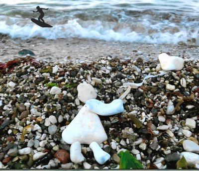 Figur aus Kieselsteinen am Strand mit Wellen und einem Surfer.