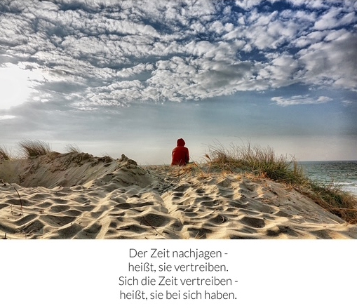 Frau sitzt auf einer Düne und schaut aufs Meer – darunter der Spruch: „Der Zeit nachjagen - heißt, sie vertreiben. Sich die Zeit vertreiben - heißt, sie bei sich haben.“