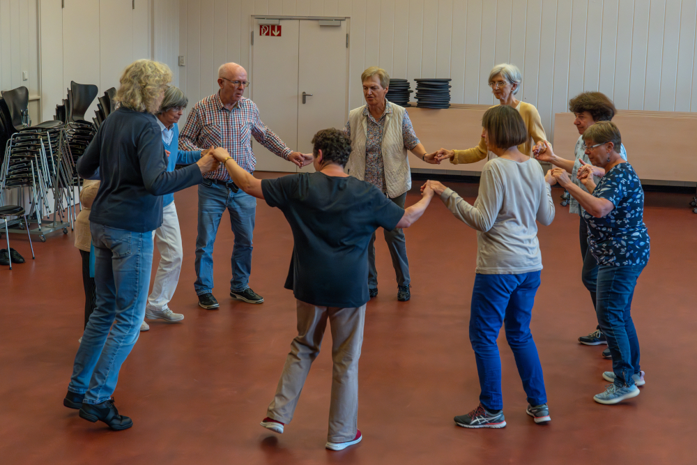 Gruppe älterer Menschen tanzt im Kreis und hält Händchen.