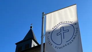 Weiße Kirchenfahne mit Logo und blauem Himmel.