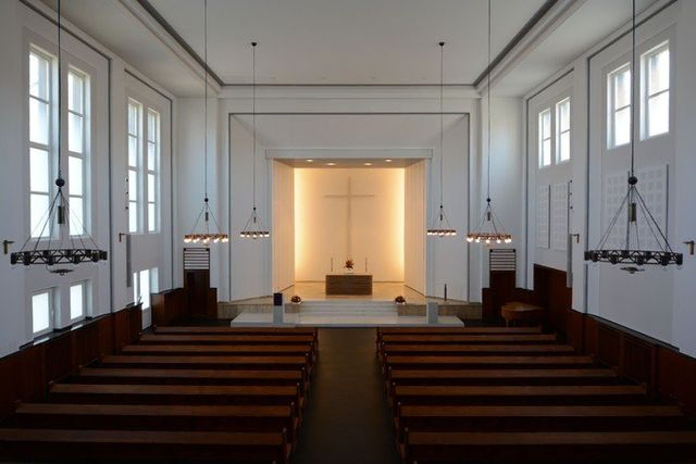 Heller Kircheninnenraum mit Altar, Kreuz und leeren Bänken.