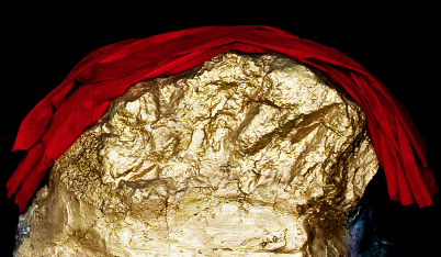 Goldene Skulptur, bedeckt mit einem roten Tuch vor schwarzem Hintergrund.