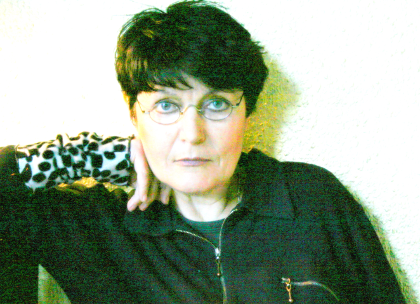 Porträt einer Frau mit Brille und kurzen, dunklen Haaren, die die Hand am Kinn hat.