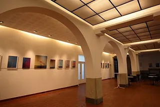 Heller Gang mit gewölbten Decken, Kunstwerken an der Wand und Tischen.